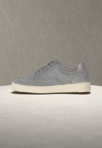 Baskets basses en daim gris avec semelle en caoutchouc couleur crème et design à lacets sur fond neutre.