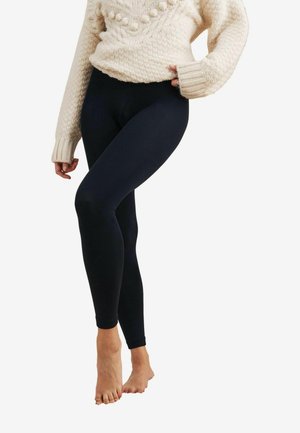 Leggings noirs en tissu extensible, avec un design ajusté qui descend jusqu'aux chevilles, associés à un pull en tricot texturé de couleur crème.