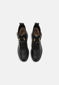 Botas de tobillo de cuero negro con ojales y herrajes dorados, puntera redonda, diseño con cordones y detalle de borde cosido. Textura suave, estilo minimalista.