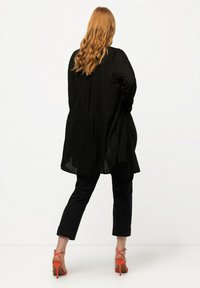 Svart texturerad lång kofta med löst snitt, i kombination med svarta byxor och orange klackar med remmar.