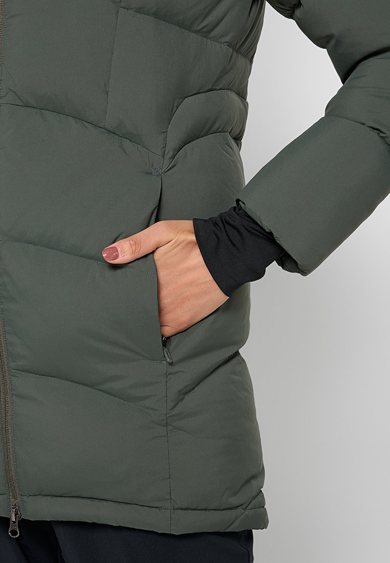 Grüne, gepolsterte Jacke mit einem Reißverschluss auf der Vorderseite, die ein horizontales Steppmuster und versteckte Seitentaschen aufweist. Der Stoff wirkt glatt und wasserabweisend.