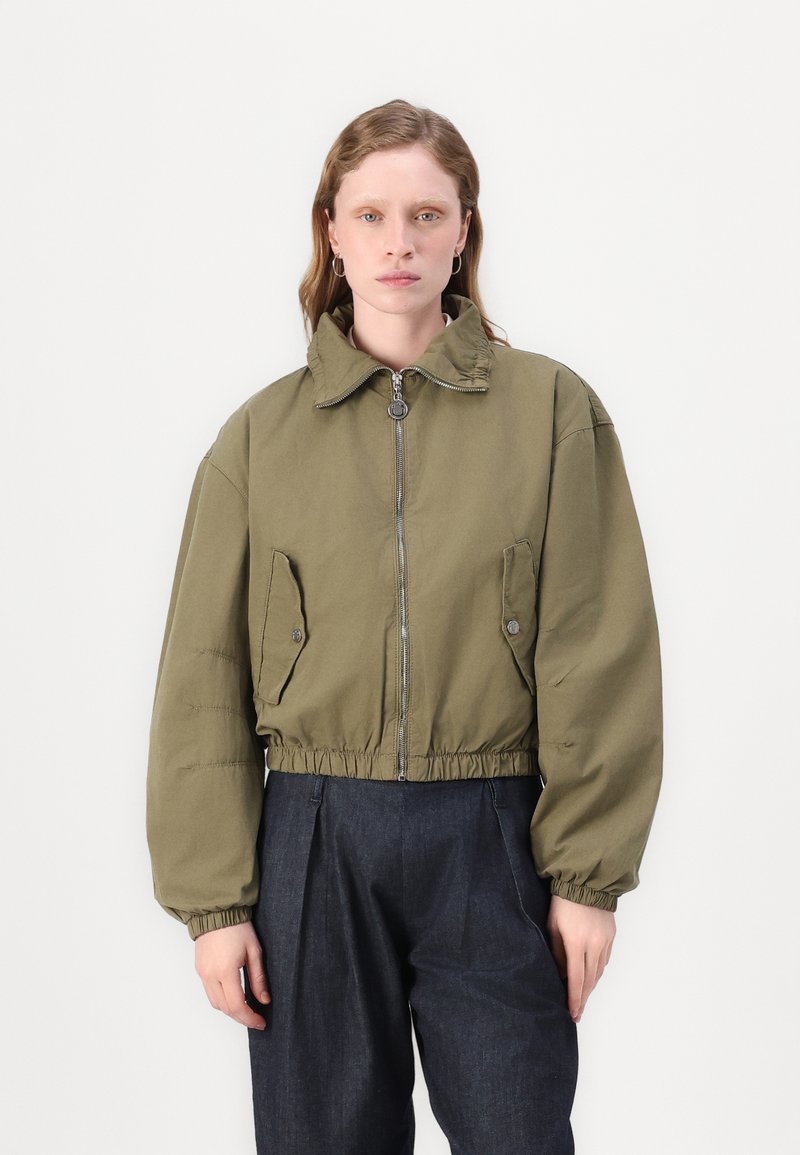 Giacca cropped verde oliva con colletto alto, zip frontale e due tasche laterali; presenta una vestibilità comoda e orlo elasticizzato.