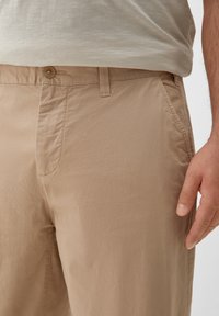 Beige katoenen broeken met een knoopsluiting, zijzakken en een zachte textuur. De stof lijkt licht en casual.