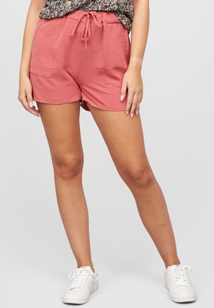 Shorts extensibles roses avec une finition texturée, dotés d'une taille élastique et d'un cordon de serrage, ainsi que de deux poches avant. Associés à des baskets blanches.
