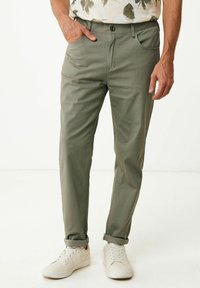 Schmale olivgrüne Hosen aus leichtem Stoff. Merkmale sind eine flache Vorderseite, fünf Taschen und umgeschlagene Säume, kombiniert mit weißen Sneakern.