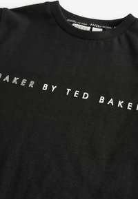 Must musträtik featuring valge tekst, mis ütleb "BAKER BY TED BAKER." Kangas on sileda tekstuuriga ja ümmarguse kaelusega.