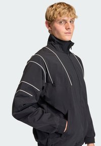 Black zip-up jacket made of lightweight material. Features white accent stripes on sleeves, stand-up collar, and side pockets.