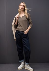 Beige ribbed top, tummansiniset leveät farkut, käännetyt hihnat ja kermaiset lenkkarit. Yllään vaaleanvärinen tekoturkis takki heitettynä yhdelle olalle.