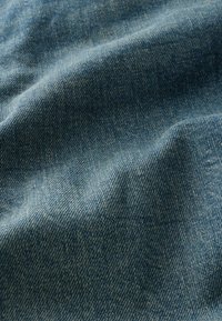 Denim-kangas keskisinisenä, hienosti kudottu hieman teksturoituneella pinnalla. Siinä on pehmeitä laskoksia ja tasainen, hillitty kiilto.