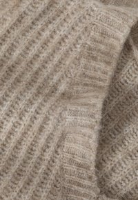 Beige gebreide stof met een gestructureerd patroon, met een zachte en fluweelachtige uitstraling. Het materiaal heeft zichtbare vezels die diepte toevoegen.