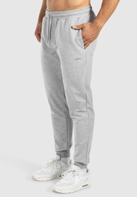 Pantalon de survêtement gris avec taille réglable par cordon, poches latérales, jambes fuselées et un discret logo sur la cuisse. Matière en coton doux.