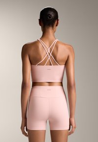 Svetlo roza atletski crop top s križnimi naramnicami, v kombinaciji z ujemajočimi se visokimi kratkimi hlačami, obema iz teksturiranega, raztegljivega materiala.