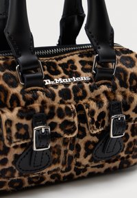 Bolsa de mão com padrão de pele de leopardo, alças em couro preto, fivelas prateadas, fecho em zíper e uma placa prateada com o logotipo da Dr. Martens.