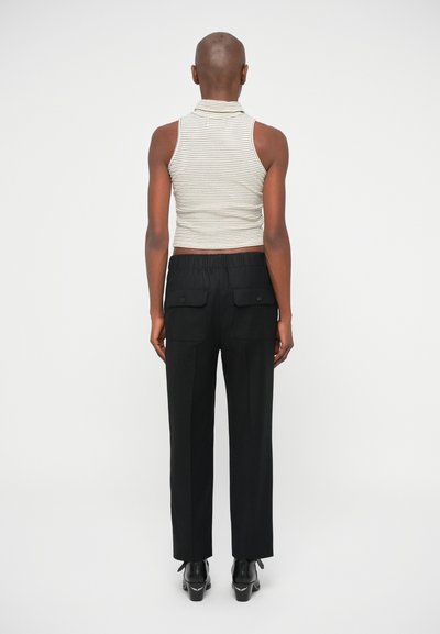 Top sem mangas em cinza e branco com gola alta; combinado com calças pretas ajustadas com bolsos laterais e um cós elástico.