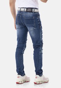 Skinny-fit, ausgefranste blaue Jeans aus Denim mit strukturiertem Finish, ausgestattet mit einem schwarzen Gürtel mit Nieten, verstellbaren seitlichen Taschen und einer mittelhohen Taille.
