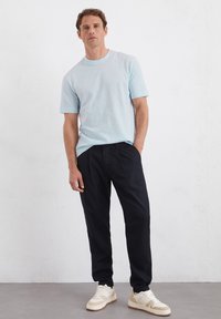 Lichtblauwe korte mouwen t-shirt, relaxed fit, gecombineerd met zwarte broeken en beige sneakers met textuurelementen. Eenvoudige, casual outfit.
