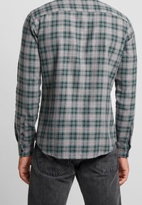 Grijze geruite shirt met groene en rode accenten, lange mouwen en een gebogen zoom. Gemaakt van ademende stof, met knoopmanchetten.