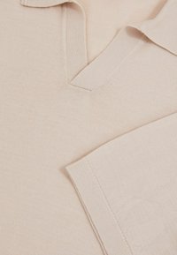 Ljusbeige pikétröja i mjukt tyg med klassisk krage, med V-ringning och korta ärmar. Slät textur, utan mönster.