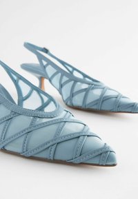Lysblå slingback hæle med spids tå, der har krydsede stropper og en slank hæl, lavet af bløde tekstil- og syntetiske materialer.