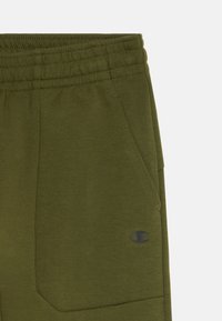 Pantalones de chándal verde oliva con cinturilla elástica, bolsillos laterales y un pequeño logo negro de Champion en el bolsillo derecho.