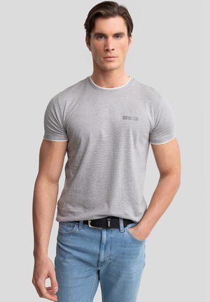 Grå kortærmet t-shirt med hvid kravekant, prydet med et logo på brystet, parret med lyseblå jeans og et sort bælte.