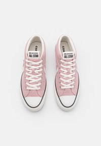 Light pink canvas sneakers with white laces, rubber toe cap, and black trim. Features a classic shape and Converse logo on the tongue.