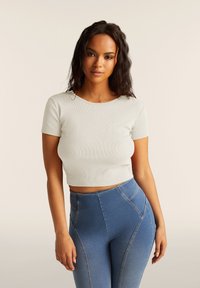 Top corto de canalé gris claro con mangas cortas, combinado con unos vaqueros azules de cintura alta que presentan costuras en contraste y costuras ajustadas.