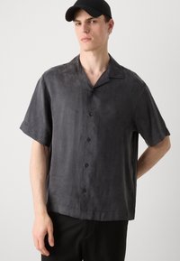 Camisa de manga corta, abotonada en gris oscuro, hecha de un tejido suave con un corte relajado y un cuello con muesca. Los botones negros completan el diseño.