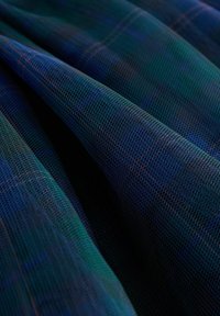 Strukturierter Stoff in dunkelgrünem und blauem Karo, mit einer netzartigen Webart und orangefarbenen Fäden, die geschichtete Falten und Tiefe zeigen.