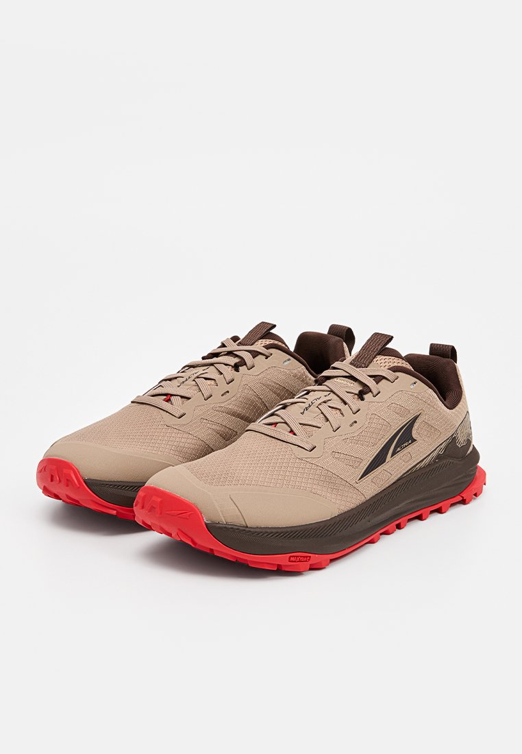 Zapatillas de trail running en tono marrón con acentos en marrón. Cuentan con un upper texturizado, lengüeta acolchada y una suela de goma roja para mejorar la tracción.