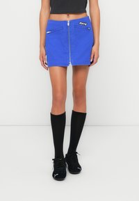 Blauwe denim mini-jurk met een ritssluiting aan de voorkant en twee ritszakken. Gecombineerd met kniekousen in het zwart en zwarte sneakers.