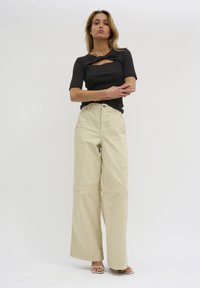 Zwarte geribbelde top met een uitsnede aan de voorkant, gecombineerd met beige wijde cargo pants met zijvakken en een zachte textuur.