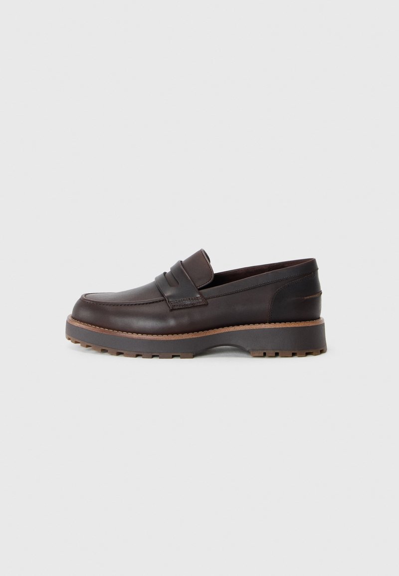 Mocassins en cuir marron avec un profil bas, présentant des coutures décoratives, une semelle en caoutchouc légèrement surélevée et une finition lisse.
