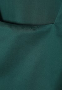 Fauteuil en tissu vert foncé avec un dossier légèrement courbé et une assise douce et rembourrée dans un design simple.