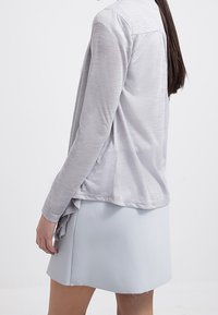 Jasnoszary, długi rękaw, bluzka o fakturowanym materiale i warstwowym wykończeniu, w zestawieniu z jasnoniebieską spódnicą o prostym kroju i postrzępionym dolnym wykończeniu.