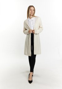 Térdhez érő, nyitott elől cardigan krémszínű kötött anyagból, texturált mintázattal és bordázott mandzsettákkal, fekete, slim-fit nadrággal és magassarkúval párosítva.