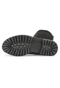 Suela de bota de goma negra con surcos profundos, con una superficie texturizada y un talón reforzado. Banda elástica lateral para mayor flexibilidad.