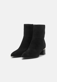 Stivaletti neri in suede con punta affusolata. Presentano un tacco a blocco in nero e oro con texture. Design semplice, finitura liscia e chiusura con cerniera.