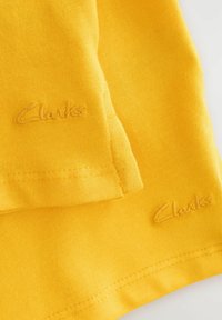 Żó�łta bawełniana tkanina o gładkiej fakturze, z przeszytym brzegiem i wytłoczonym logo "Clarks" w dopasowanej żółtej nici.