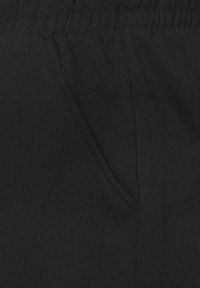 Schwarze Jogginghosen aus weichem Stoff, mit einer Seitentasche und einem elastischen Bund für zusätzlichen Komfort. Glatte Textur mit feinen Nähdetails.