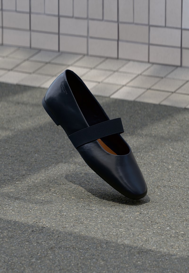 Črne usnjene ravne čevlje z zaobljenim nosom, ki imajo mehko črno elastično naramnico čez vamp. Gladka tekstura in minimalističen dizajn.