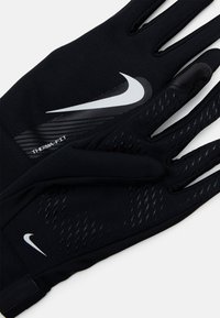 Guantes térmicos en negro con un diseño elegante. Las características incluyen una superficie texturizada, acentos de silicona y logotipos reflectantes de Nike.