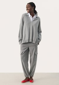 Grå oversized trøje med V-hals, parret med grå cargo bukser med sidelommer. Livlige røde flade sko fuldender outfittet.