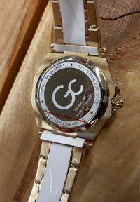 Orologio in acciaio inossidabile con rifinitura dorata, quadrante rotondo bianco, cinturino in silicone bianco, dettagli incisi sul retro e impermeabilità.