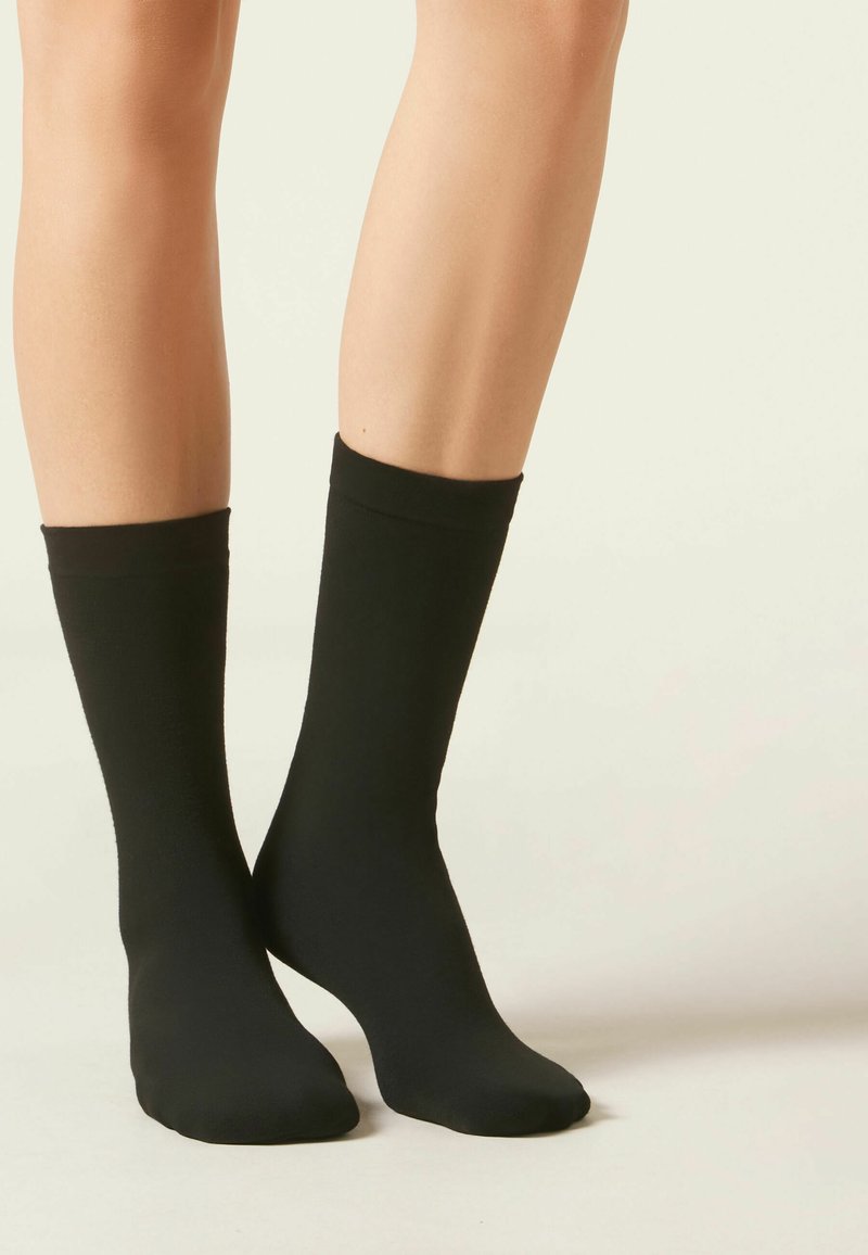 Calcetines negros hasta el tobillo, hechos de una tela suave, cuentan con una banda superior ribeteada y un diseño de punta sin costuras para mayor comodidad y flexibilidad.