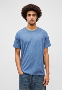 Sinine heegeldatud lühikeste varrukatega T-särk, mis on valmistatud pehmest puuvillakangast, ringkaelusega ja rinnal on väikene punane Levi'si logo.