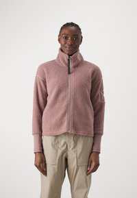 Pink fleece jacket with a high collar, full front zipper, and soft texture. Features long sleeves and a relaxed fit. Paired with beige cargo pants.