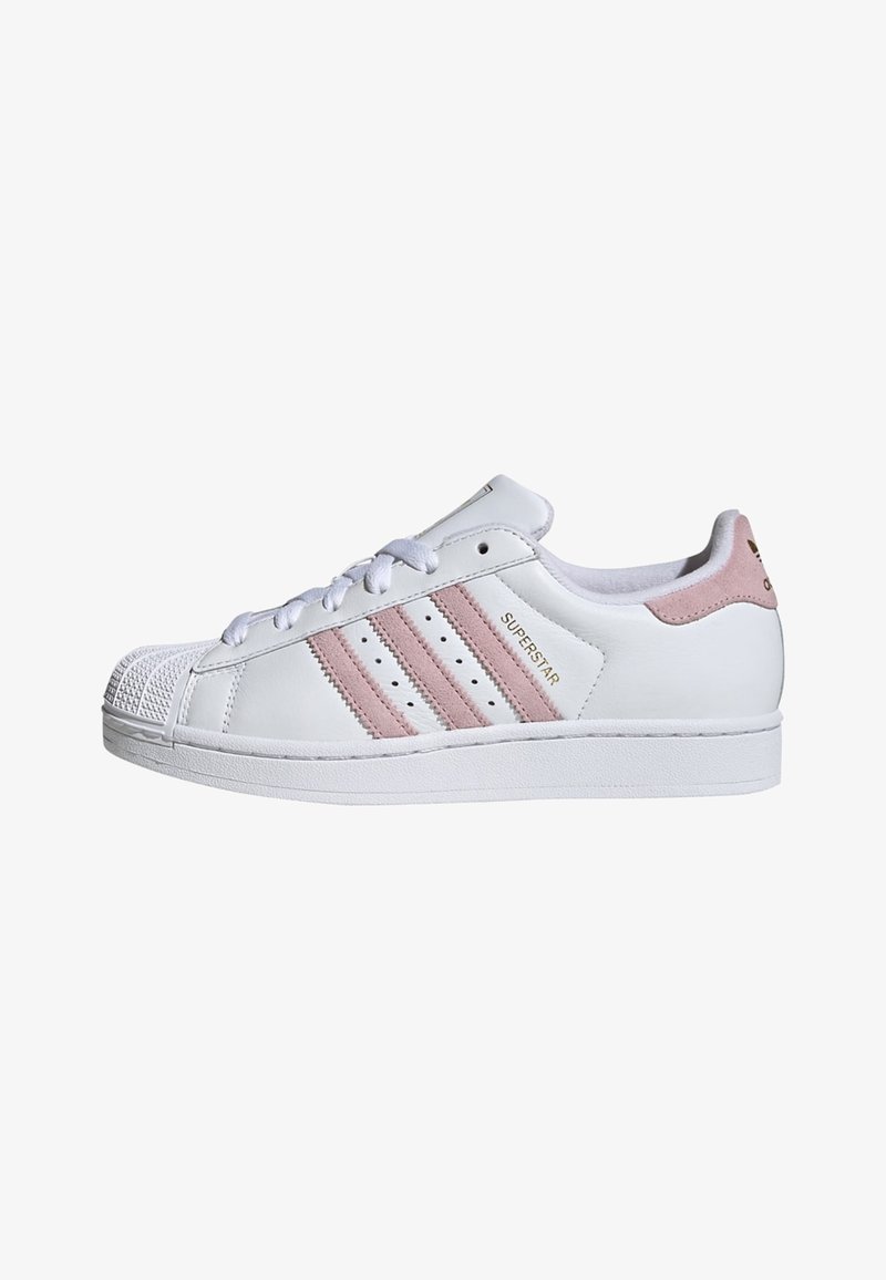 Λευκό low-top αθλητικό παπούτσι με ανοιχτό ροζ ριγέ, κορδόνια μπροστά, προστατευτική μύτη και ετικέτα "SUPERSTAR" στο πλάι.