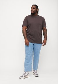 Camiseta gris de manga corta combinada con jeans rectos de lavado claro. Llevada con zapatillas gris y blancas. Diseño sencillo sin patrones.