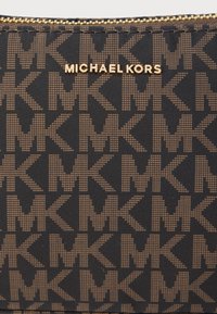 Smeđa torbica od najlona s uzorkom s cjelokupnim "MK" logotipom, zlato obojanim patentnim zatvaračem i utisnutim natpisom "MICHAEL KORS" u zlatu.